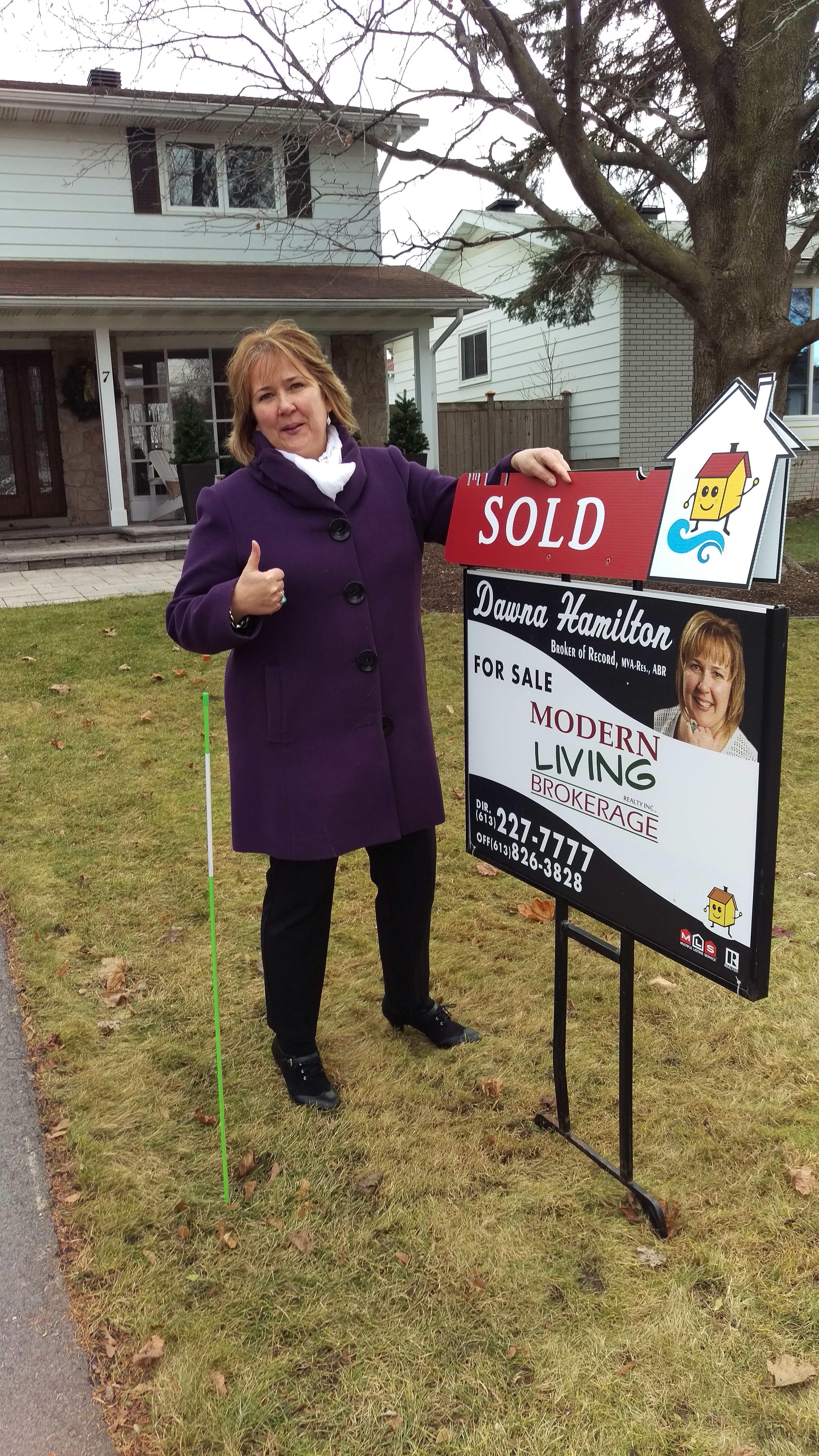 Dawna Hamilton standing beside a Modern Living Realty Brokerage sign with the words SOLD